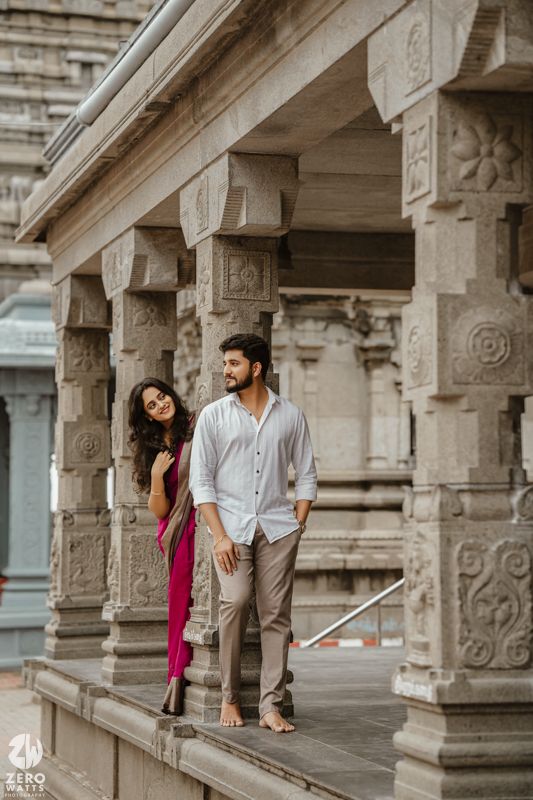 A couple in traditional Indian attire poses elegantly in a temple corridor with ornate stone pillars.