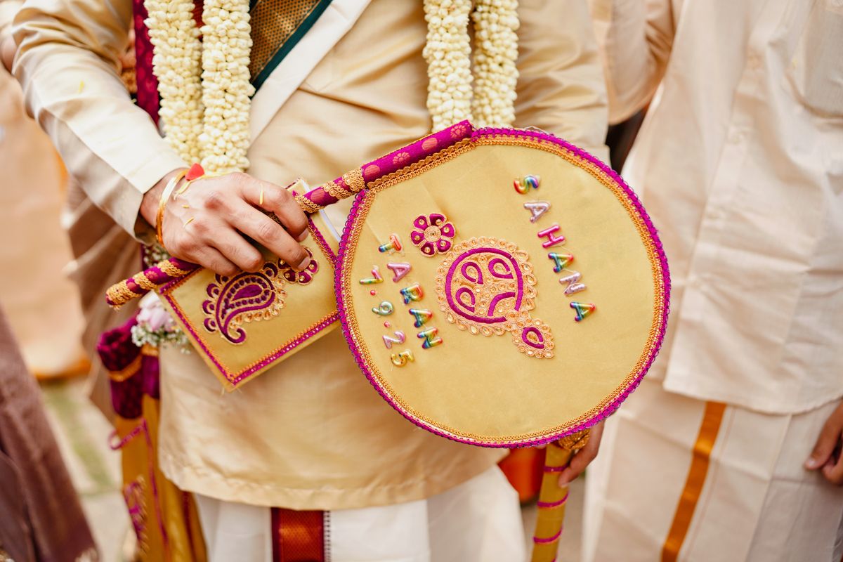 Traditional Indian wedding decorations featuring hand-held fans with ornate pink and gold designs.