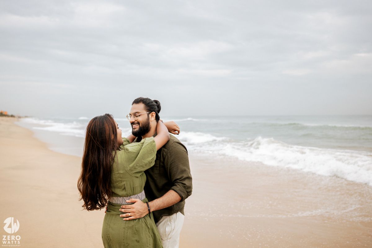 A romantic couple embraces on a peaceful beach with waves crashing in the background.