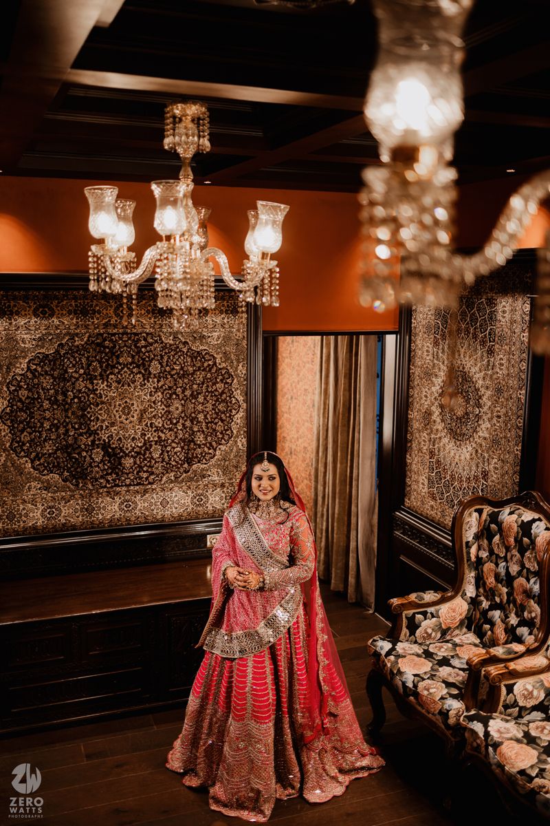 Crystal chandeliers illuminate an elegant room with ornate wallpaper and traditional Indian wedding decor.