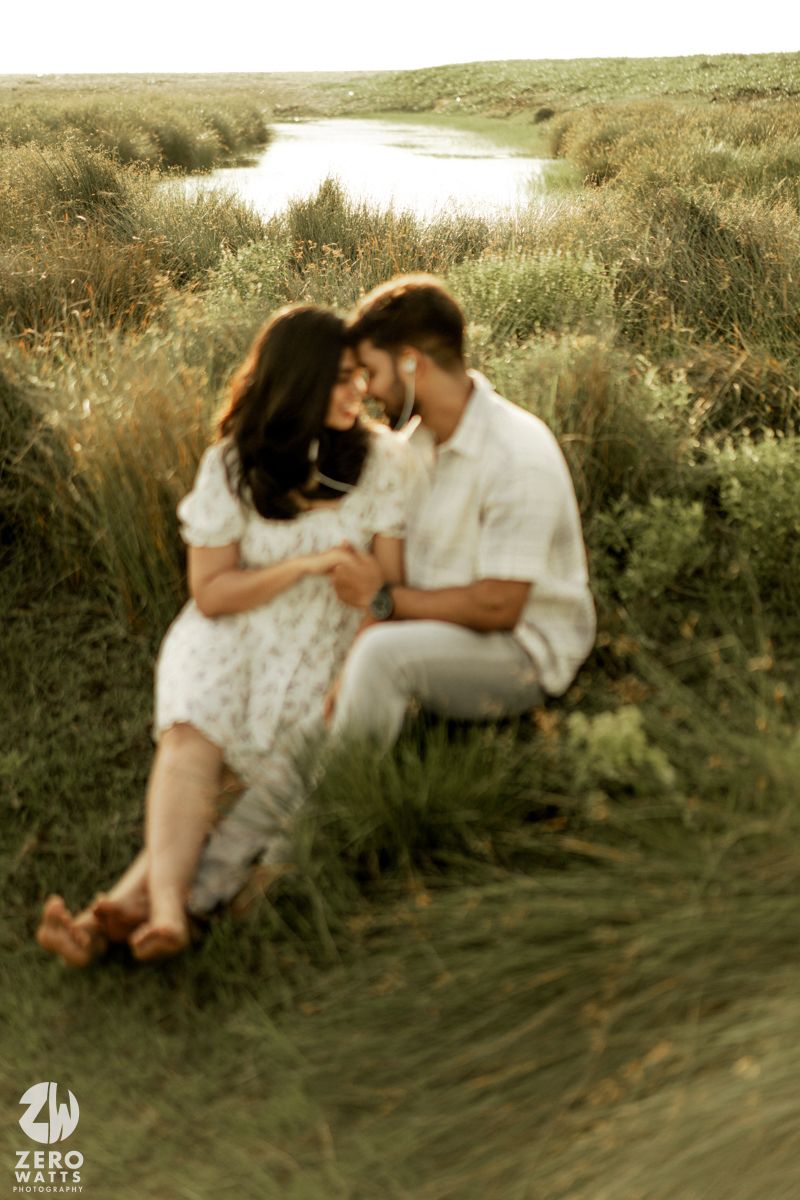 An intimate moment captured between a couple lounging in golden-lit grassland near water.