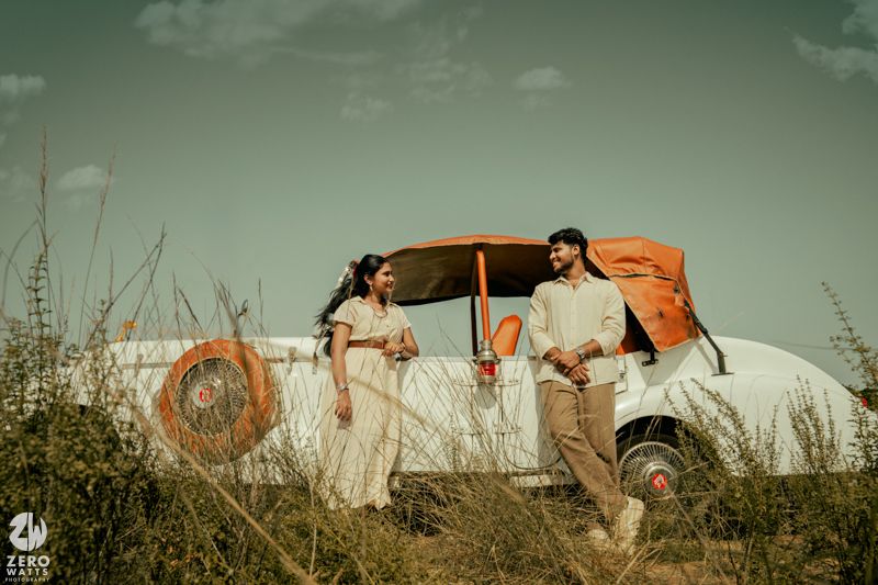 Vintage cream-colored car parked in tall grass field under moody green sky with retro styling and aesthetic.