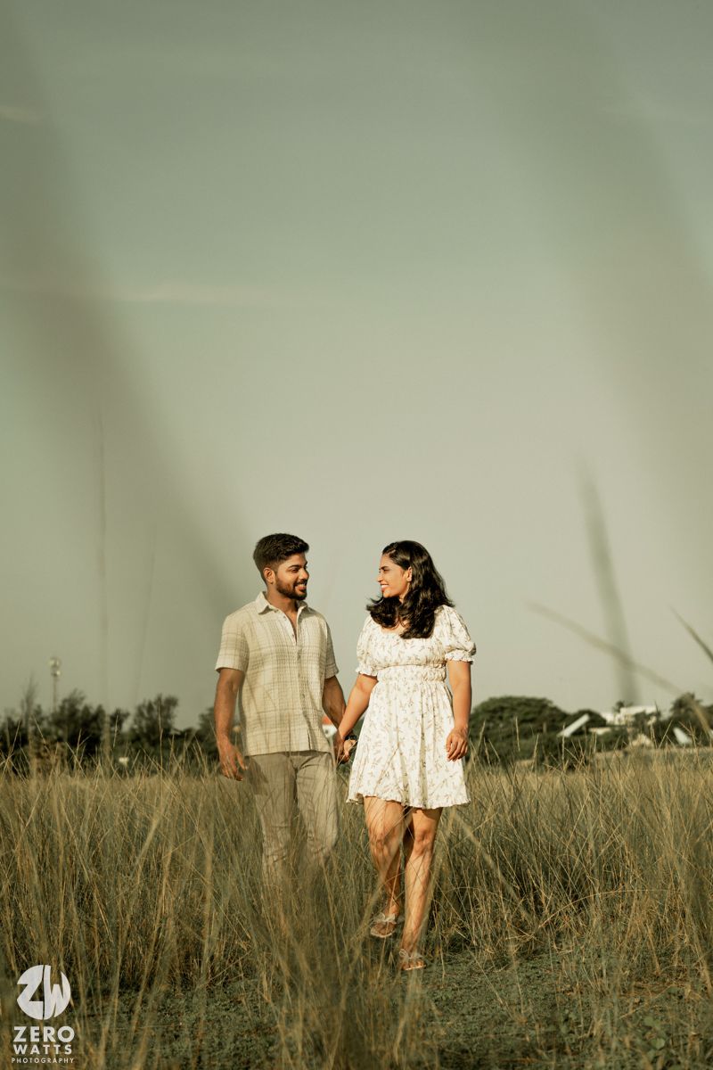 Couple in light summer outfits walking together through a serene grassland landscape.