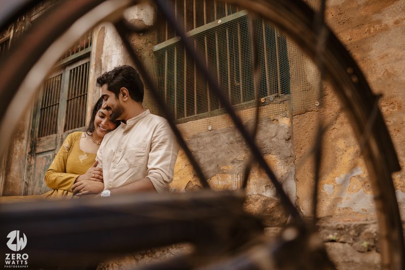 A couple sitting on a bench against a rustic brick wall with bicycles parked nearby.