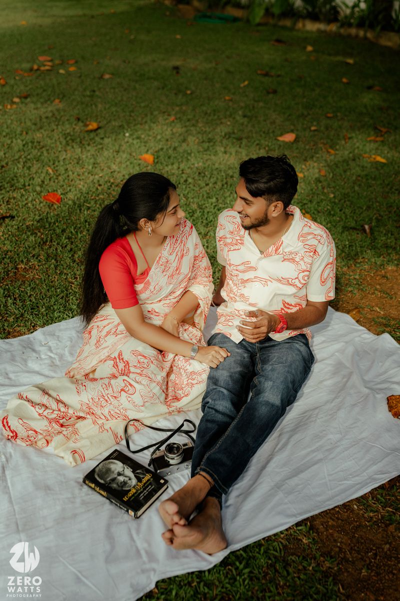 A couple relaxes on a white blanket in the grass with fallen autumn leaves scattered around them.
