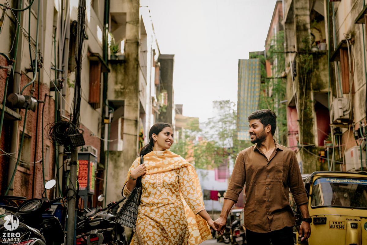 A couple walks together through a narrow urban street lined with old buildings and storefronts.