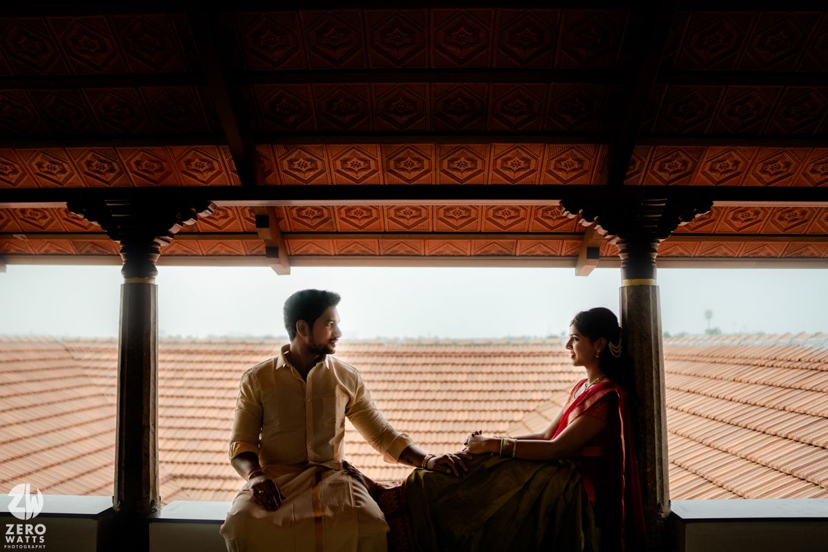 South Indian couple in traditional dress sharing a romantic moment on a wooden balcony.