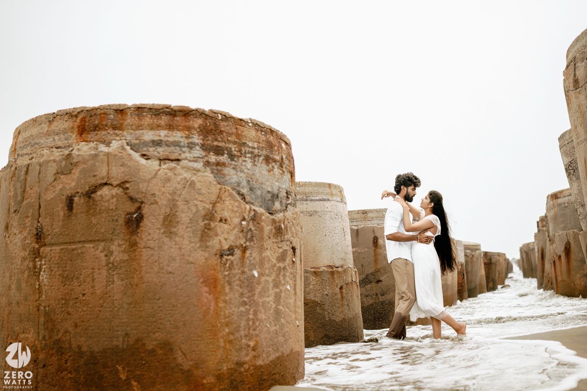Couple sharing a romantic embrace between large stone sea breakers on a misty beach shoreline.