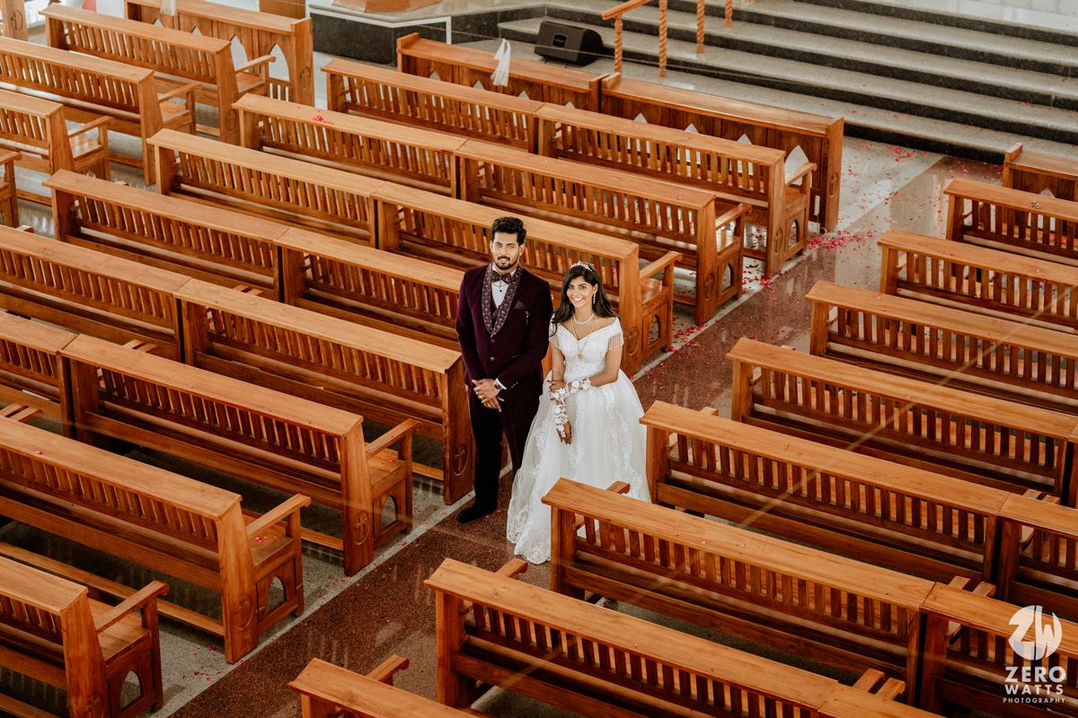 Bride and groom standing in church aisle surrounded by wooden pews, aerial view of elegant wedding ceremony.