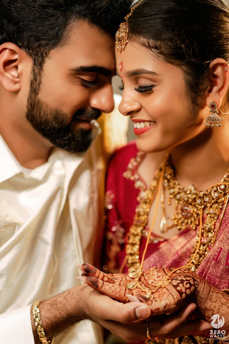 South Indian bride and groom sharing intimate moment, bride adorned with gold jewelry and mehndi hands.