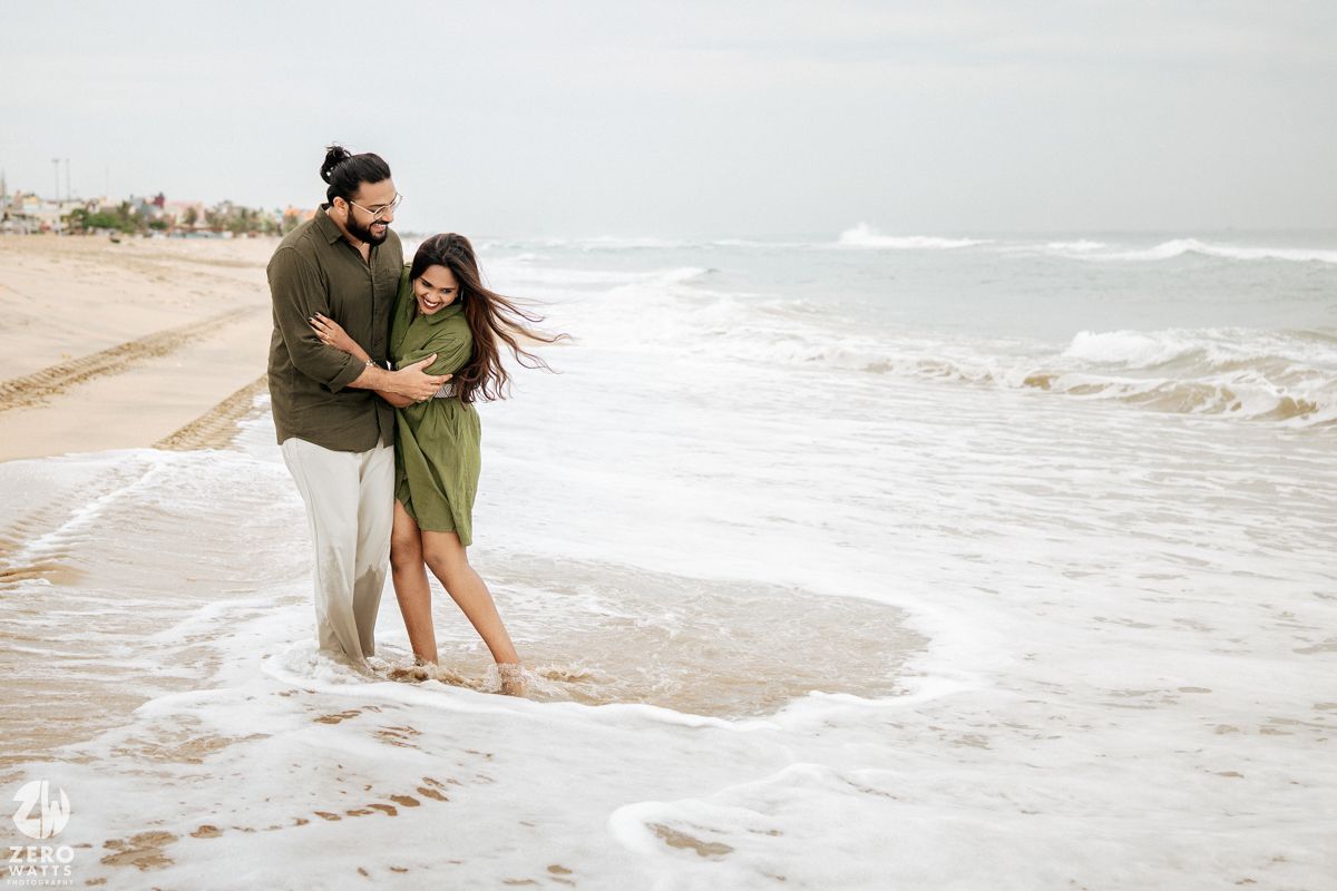 Two people share a romantic moment as ocean waves wash up on the sandy shore.