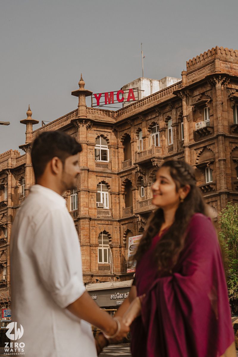 A couple stands in front of a historic building with ornate architecture and arches.