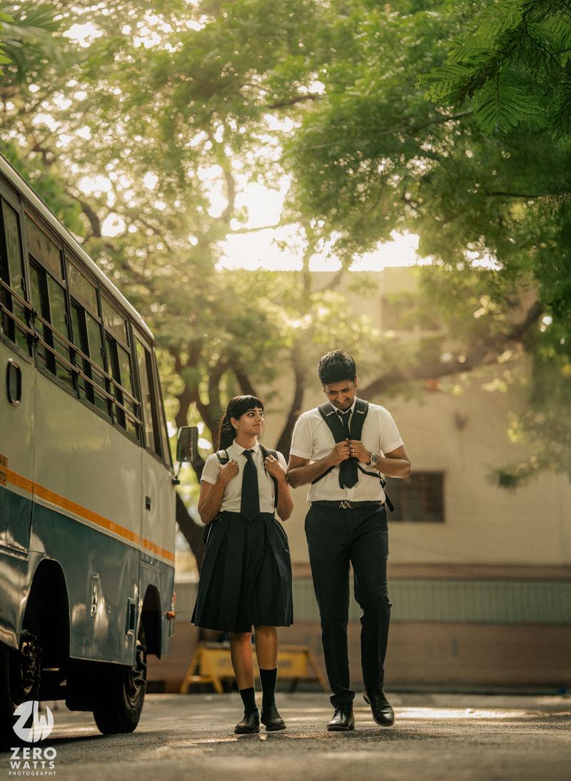 Students walking together near a parked bus on a tree-lined campus path.