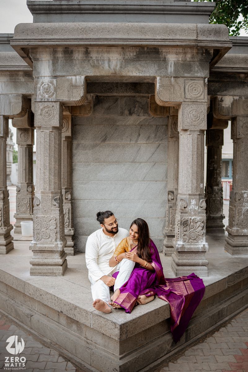 Romantic couple shares tender moments in traditional stone temple corridor with ornate pillars.