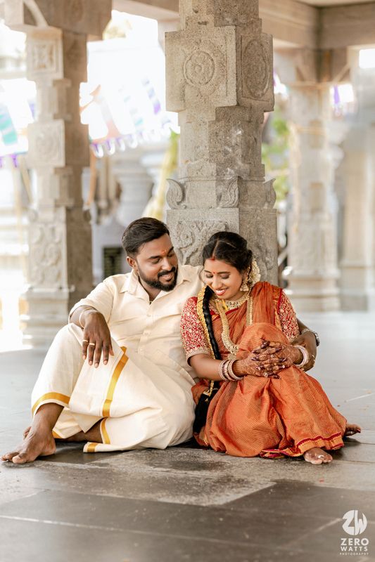 A couple in traditional Indian attire lying on a temple floor with ornate stone pillars in the background.