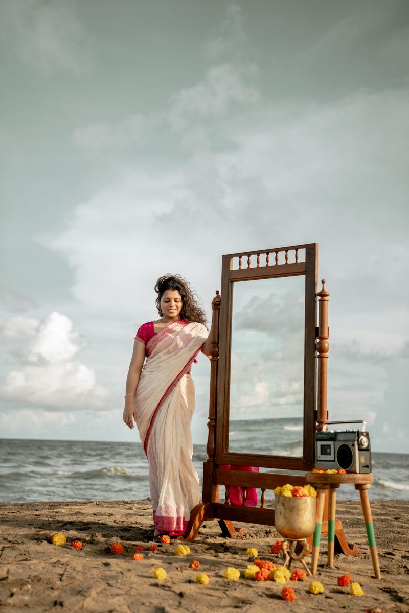 A wooden mirror frame and vintage radio set up artistically on a beach with scattered flower petals at sunset.