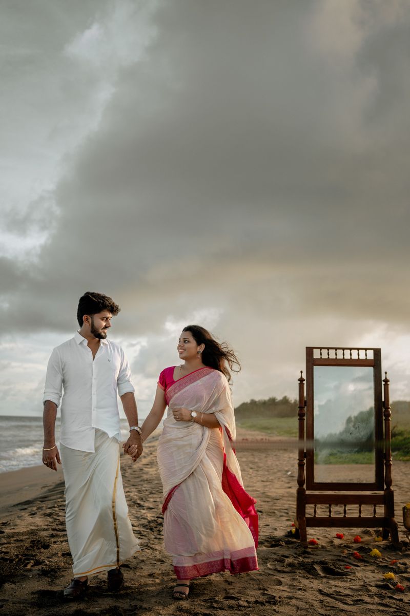 Ethereal beach photoshoot featuring a traditional wooden mirror frame and coastal decor under stormy skies.