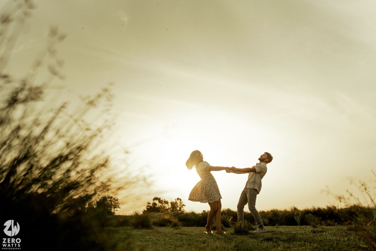 Silhouetted couple dancing in a field at sunset with tall grass swaying in the background.