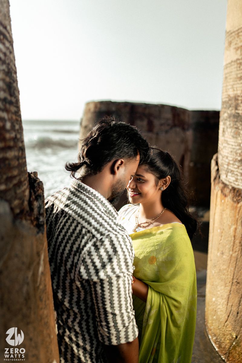 A couple shares an intimate moment between stone pillars by the ocean.