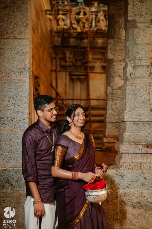 A couple in traditional Indian attire share candid moments in front of ancient temple architecture.