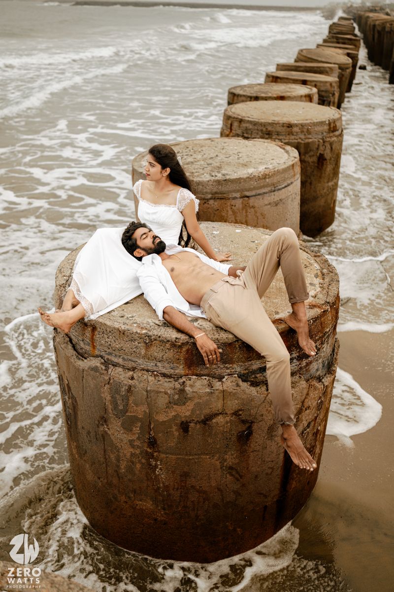 Romantic couple relaxing on concrete sea breakers with ocean waves, man in white shirt and woman in white top at beach.
