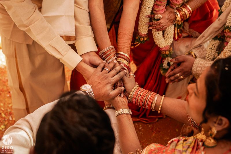Close-up of hands joined during South Indian wedding ceremony with bangles and henna.