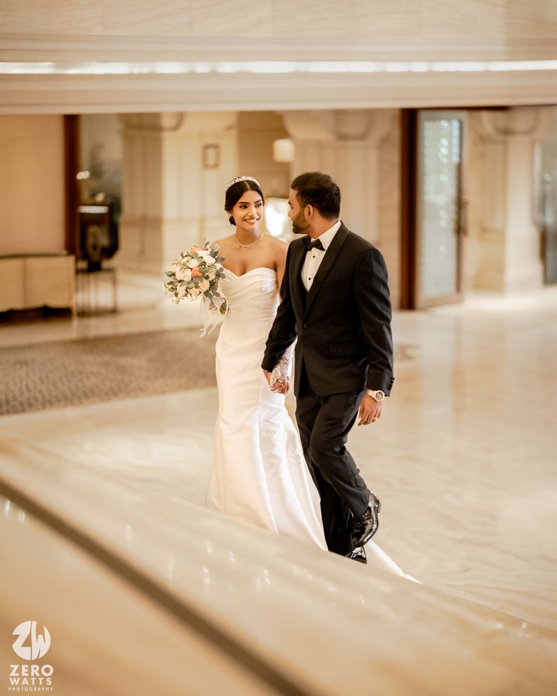 Bride and groom walk hand in hand through elegant marble hall, bride carrying a floral bouquet.