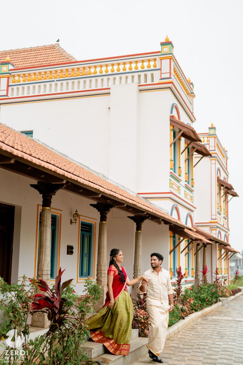 Indian couple in traditional attire walking beside a colorful heritage building with ornate architecture.