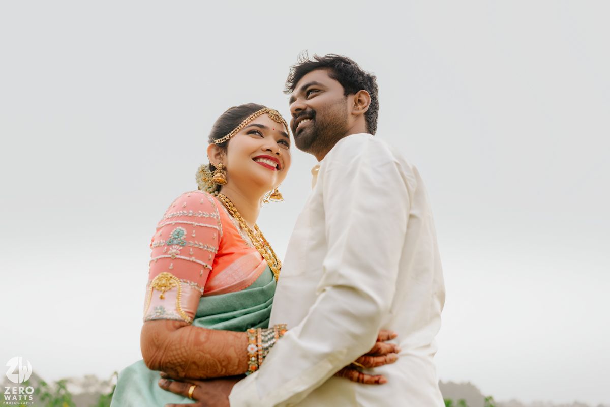 Indian couple in traditional wedding attire share romantic embrace outdoors smiling joyfully.