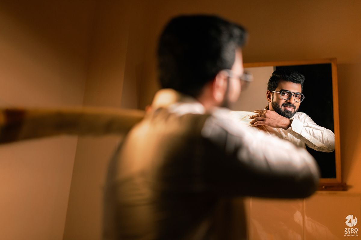 Groom in white kurta adjusting his outfit while looking in a mirror before his wedding.