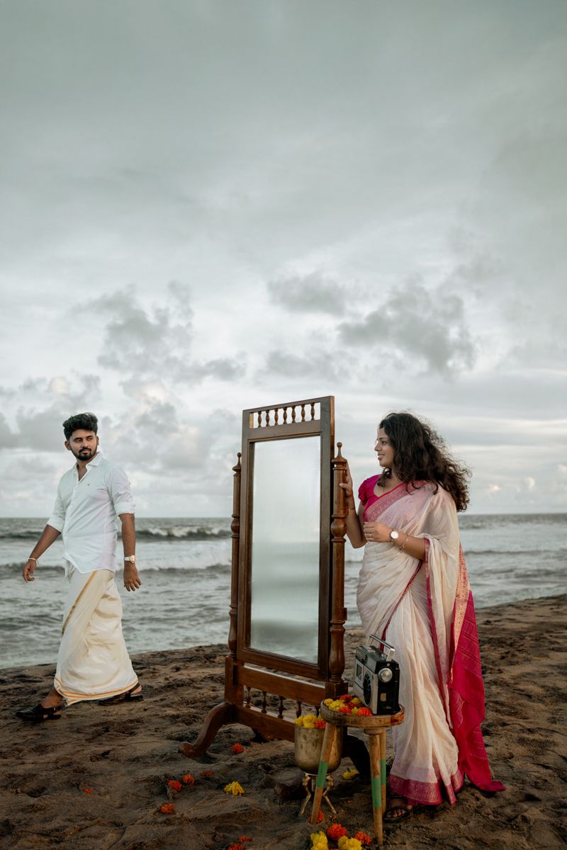 A vintage-style wooden mirror sits on a beach shore with crashing waves and cloudy skies.