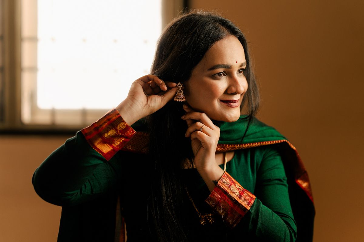 A person in a green sweater poses against a warm-toned wall with dramatic lighting and shadows.