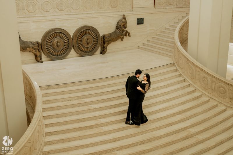 A couple shares an intimate moment on elegant marble stairs with ornate circular designs on the wall.