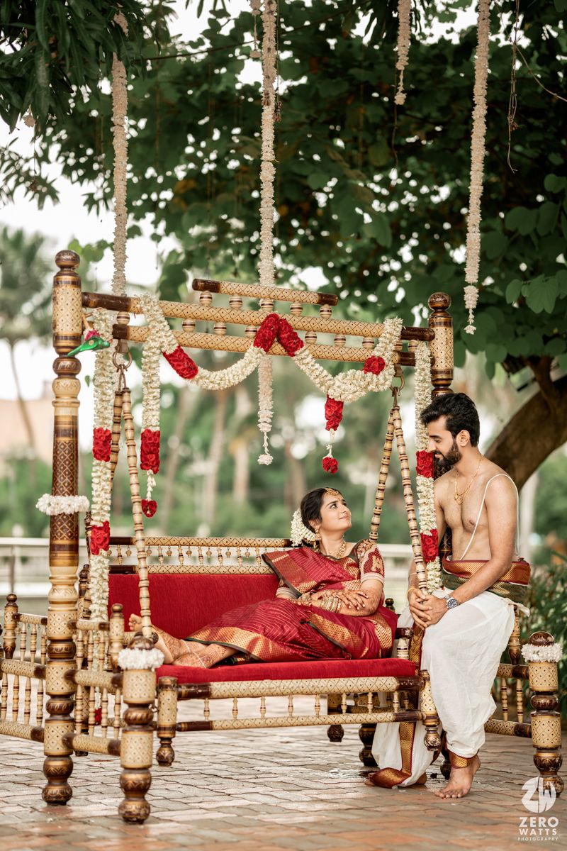 Ornate wooden swing decorated with red flowers and traditional elements at an outdoor Indian wedding.