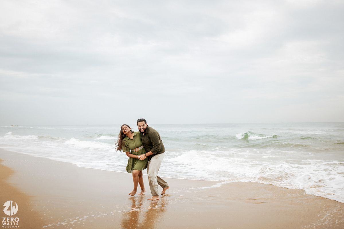 Couple sharing a romantic moment on a cloudy beach with waves rolling in.