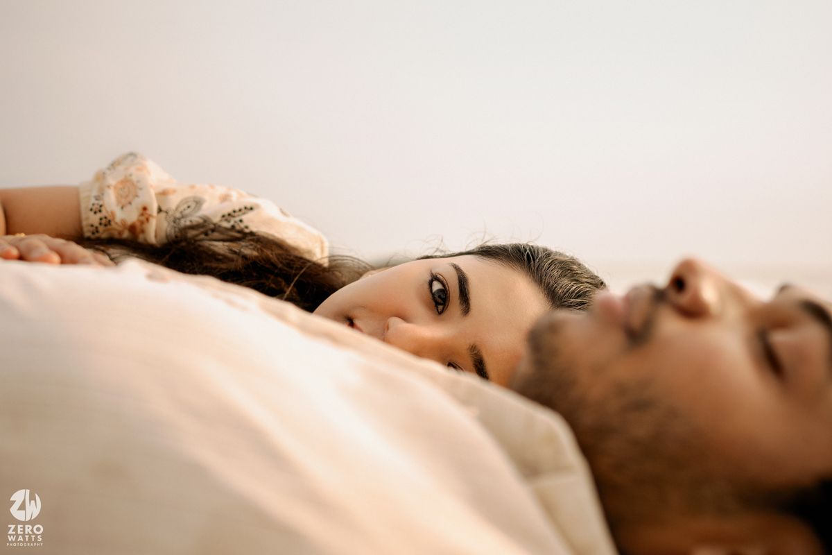 Couple shares intimate moment lying together on beach rocks during golden hour sunset.
