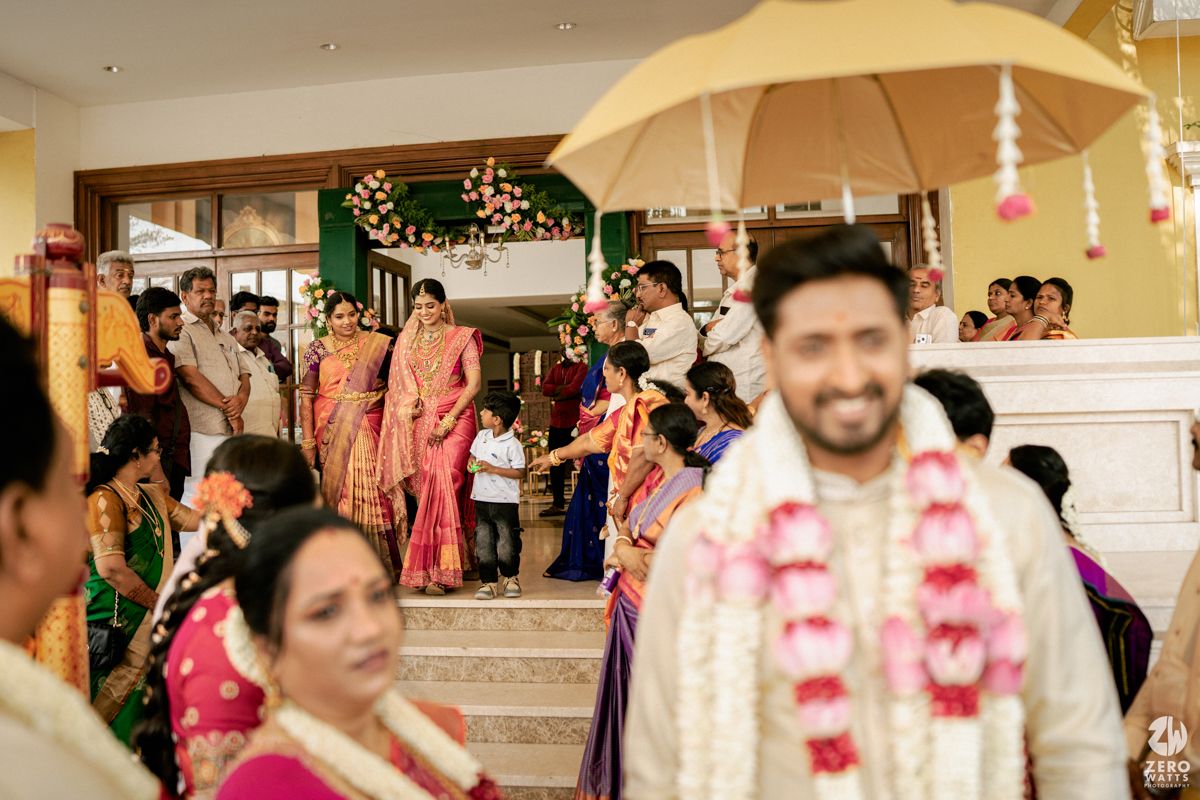 Indian bride makes grand entrance under yellow umbrella as groom awaits during traditional South Indian wedding.