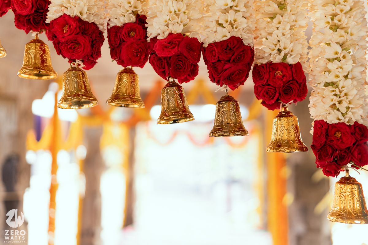 Golden bells hanging from a garland of red roses and white flowers, creating an elegant wedding decoration.