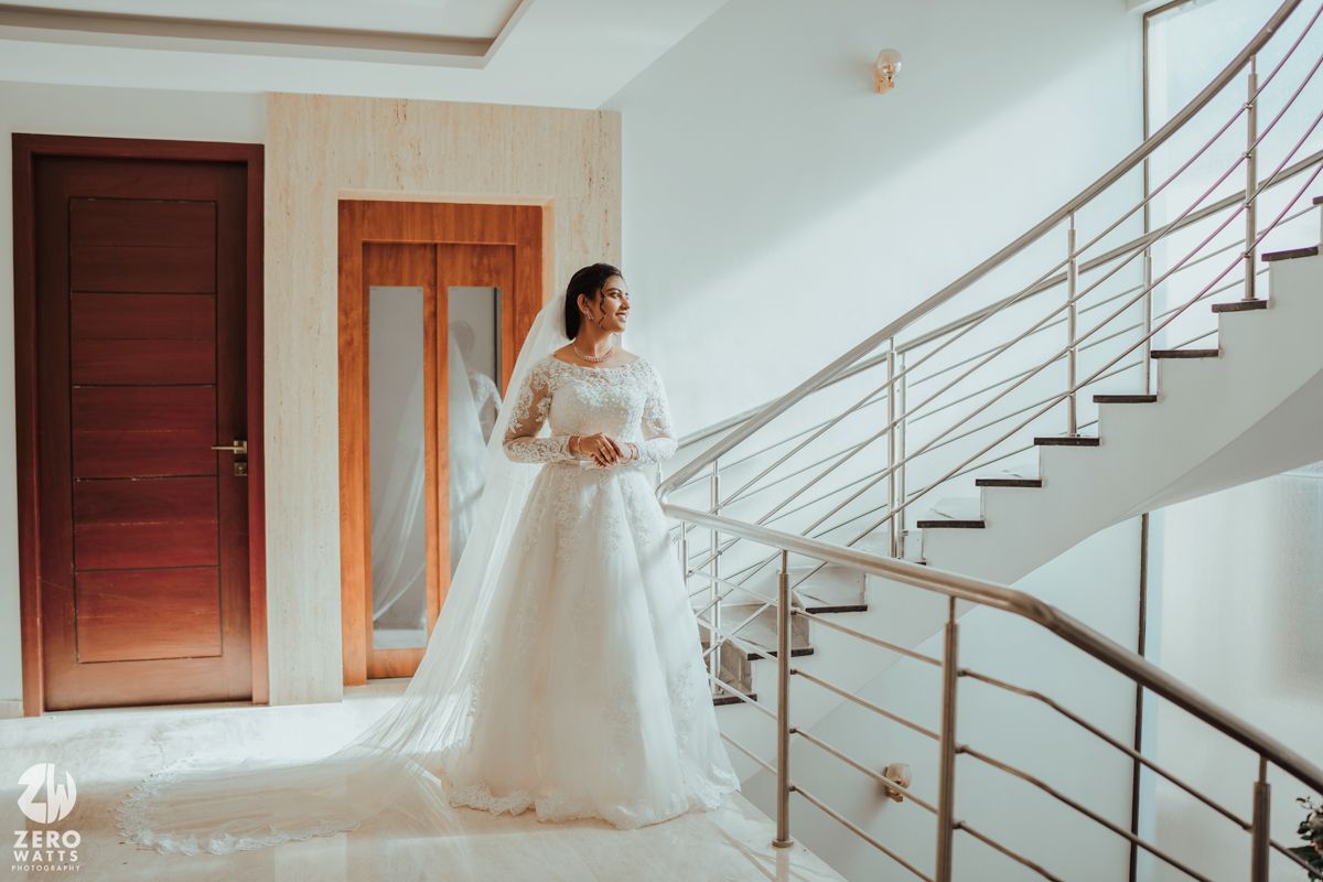 Beautiful white wedding gown with delicate lace details cascading down a modern staircase with metal railings.