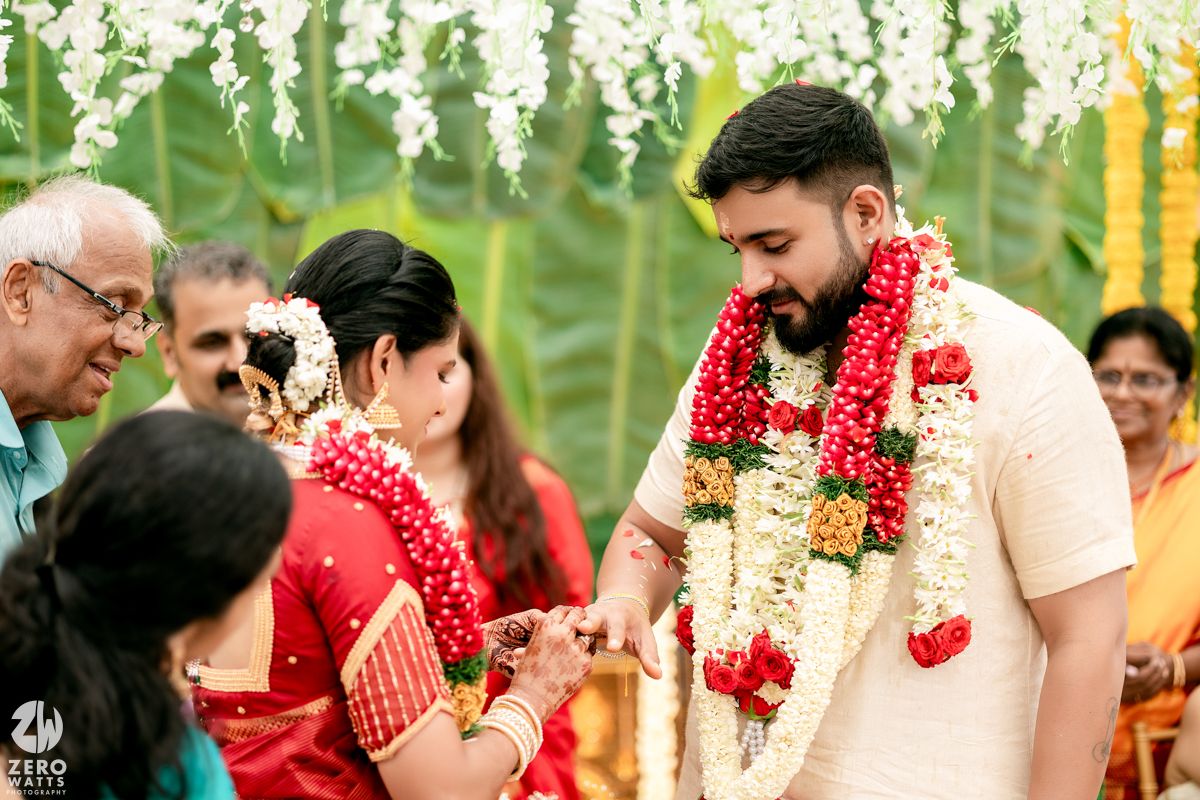 Traditional Hindu wedding ceremony with floral decorations and red garlands against a green backdrop.