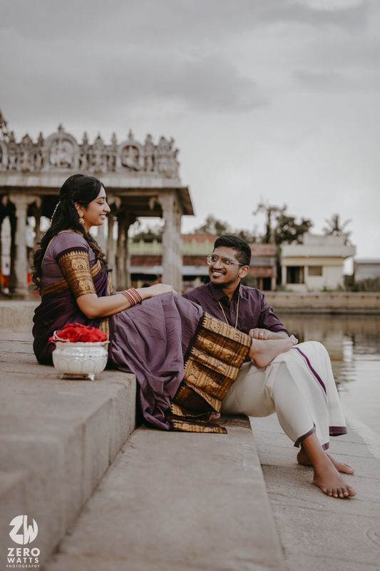 Traditional Indian couple relaxes on temple steps near water during an outdoor photoshoot.