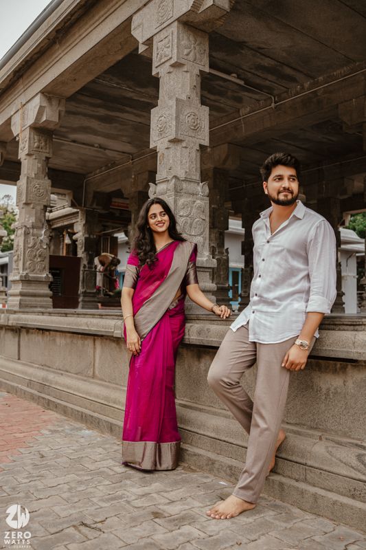 Couple poses playfully in traditional Indian temple corridor with stone pillars and archways.