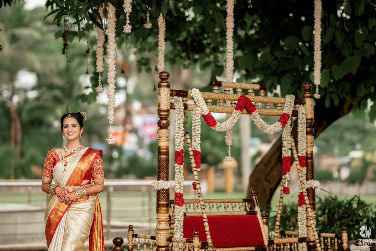 Ornate Indian wedding mandap decorated with red and gold fabric and floral arrangements in an outdoor garden setting.