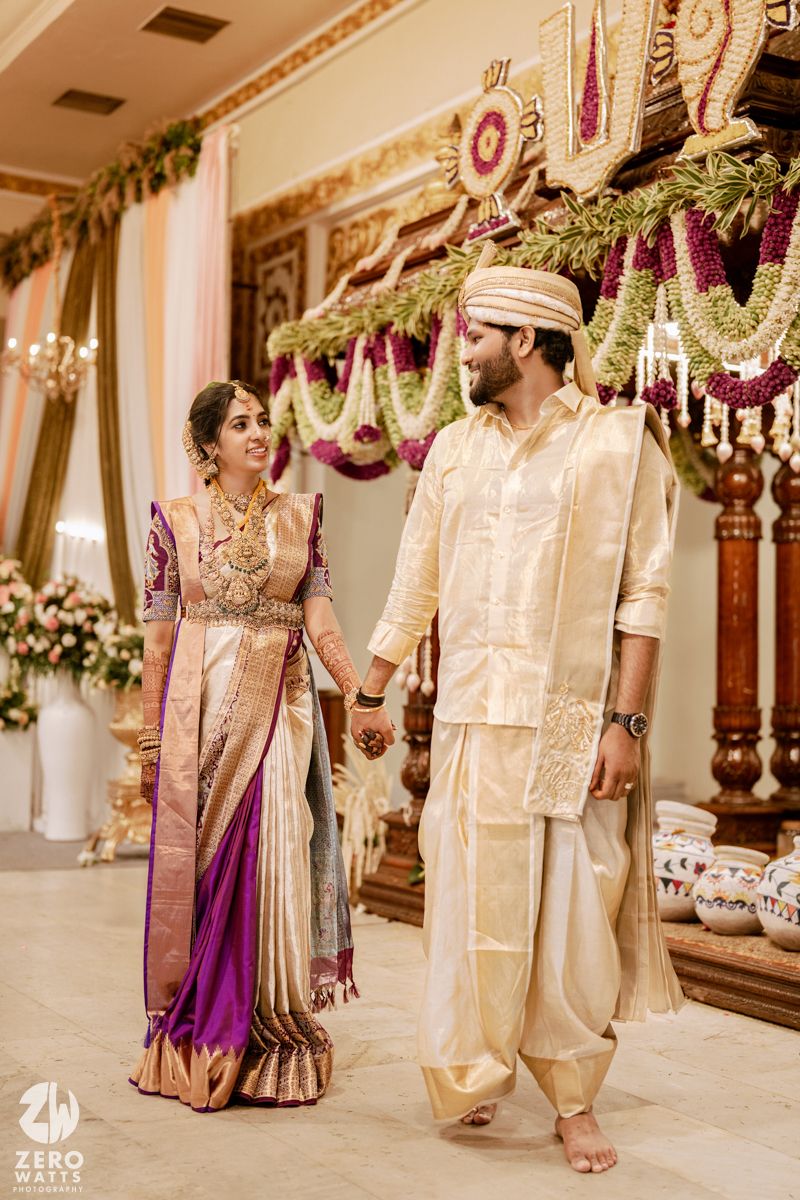 Wedding ceremony in elegant indoor venue with decorative purple and white floral arrangements hanging from above.
