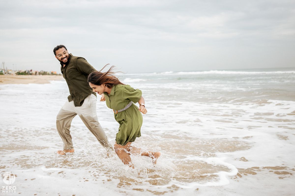 Playful couple running and jumping through the ocean surf on a foggy beach day.