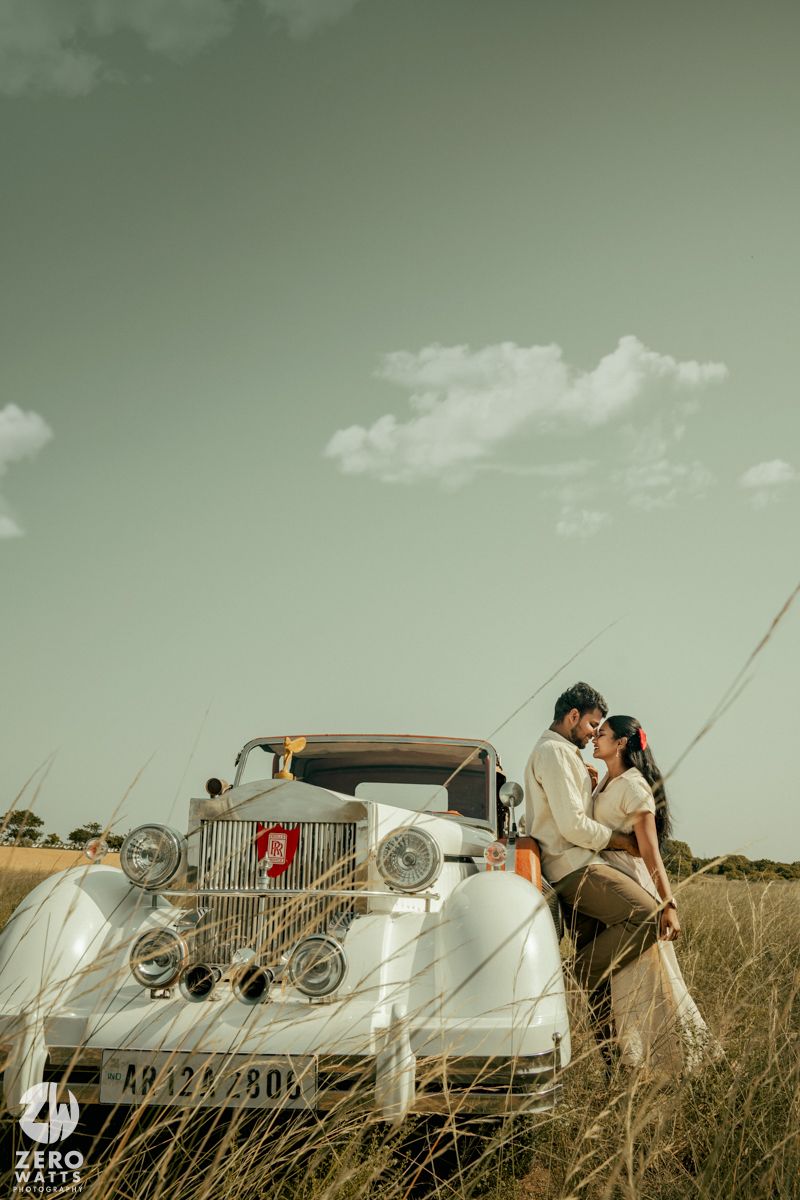 Romantic photoshoot featuring a couple and a vintage white car in tall grass under green-tinted skies.