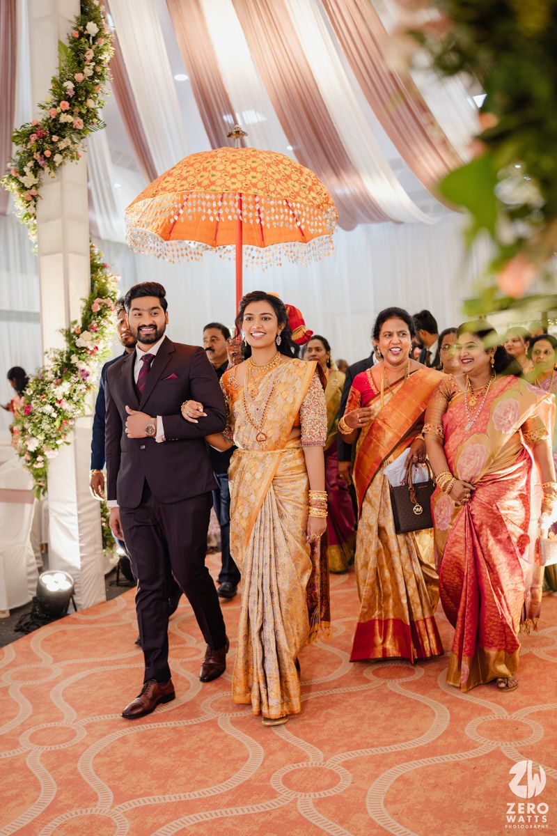 Wedding guests in traditional South Asian attire walking under decorative mandap with floral arrangements.