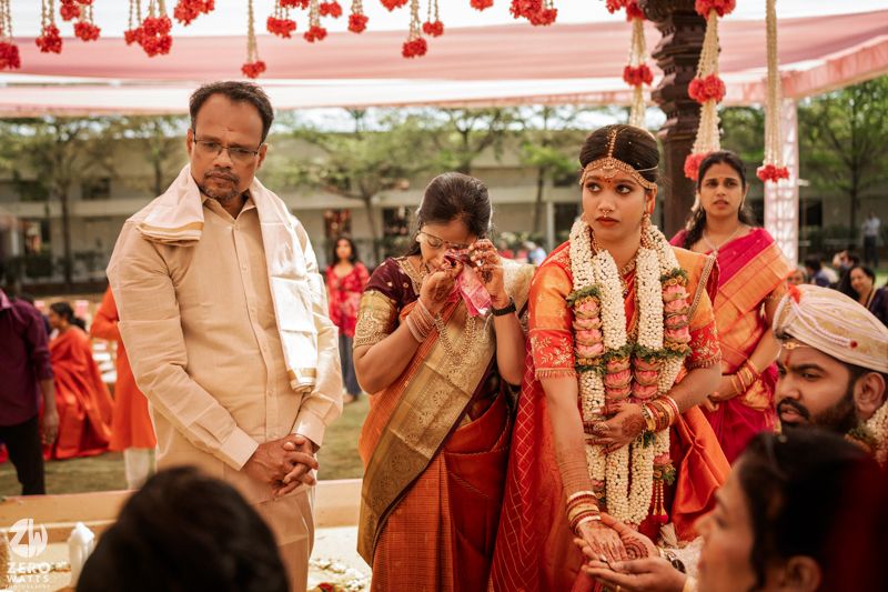 Emotional South Indian bride in red saree with family during traditional wedding ceremony.