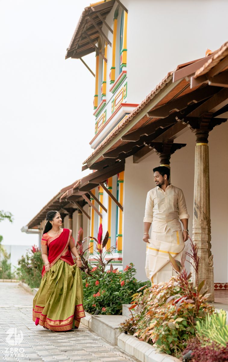 South Indian couple in traditional attire sharing a glance outside a vibrant heritage temple-style building.