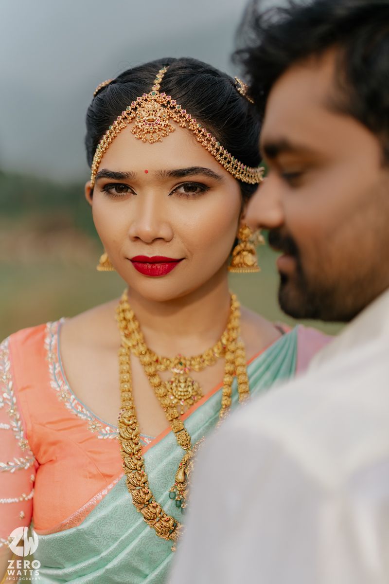 South Indian bride in mint saree with gold temple jewelry and maang tikka poses with groom during wedding shoot.